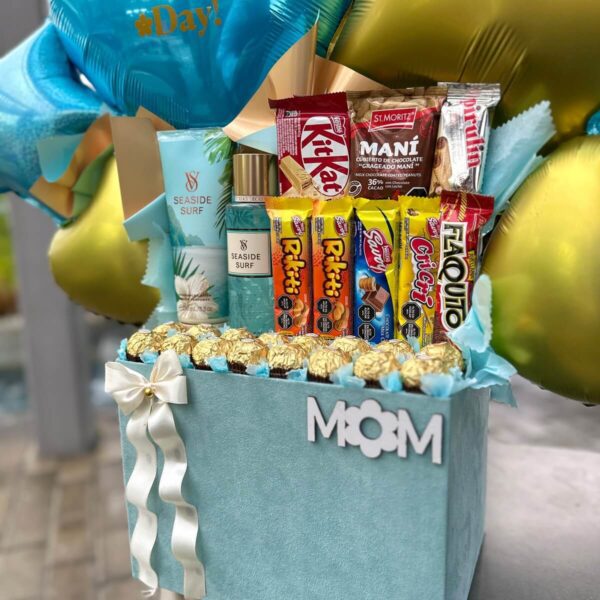 Arreglo de regalo para mamá con chocolates Ferrero, globos dorados y azules, y productos Seaside Surf.