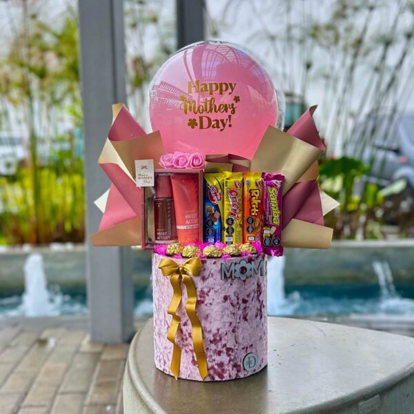 Arreglo de regalo con globo rosa, chocolates y cremas en caja circular rosa.