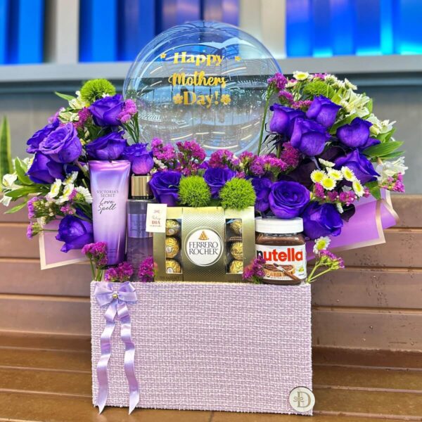 Caja decorativa con flores violetas y chocolates Vista frontal del arreglo floral con globos y dulces